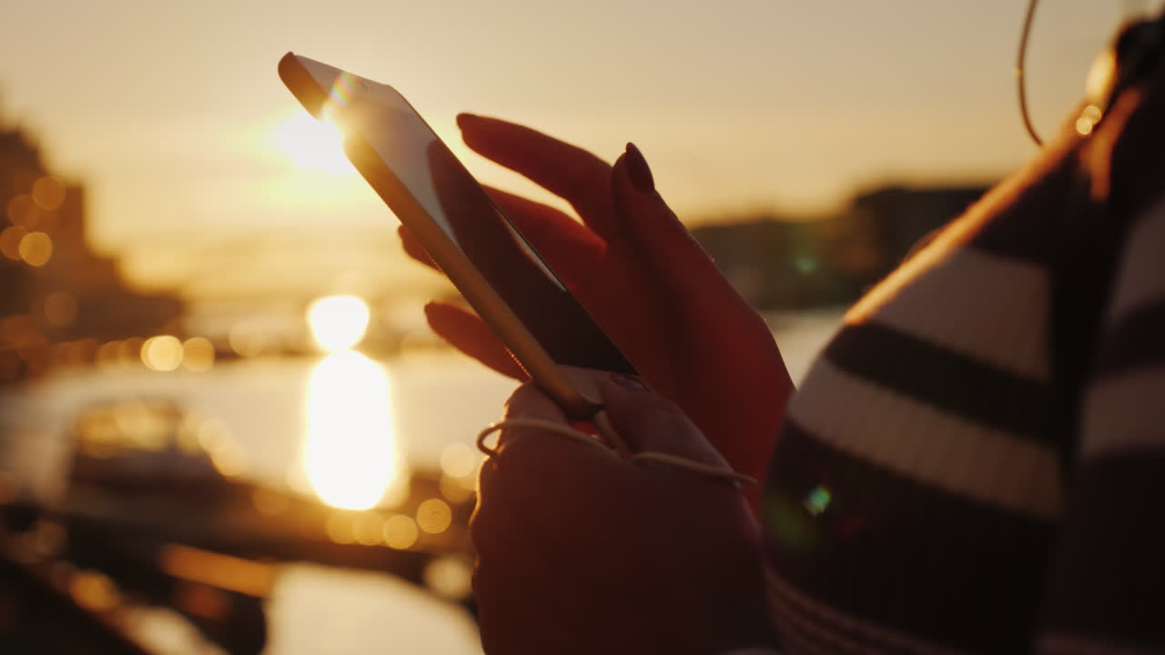 manos de una mujer con un teléfono inteligente en el fondo de un muelle con yates al atardecer 4k video