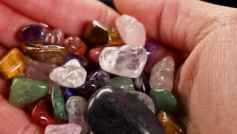 A hand holds various chakra stones, including tiger's eye and amethyst, under soft lighting, highlighting their vibrant colors and textures
