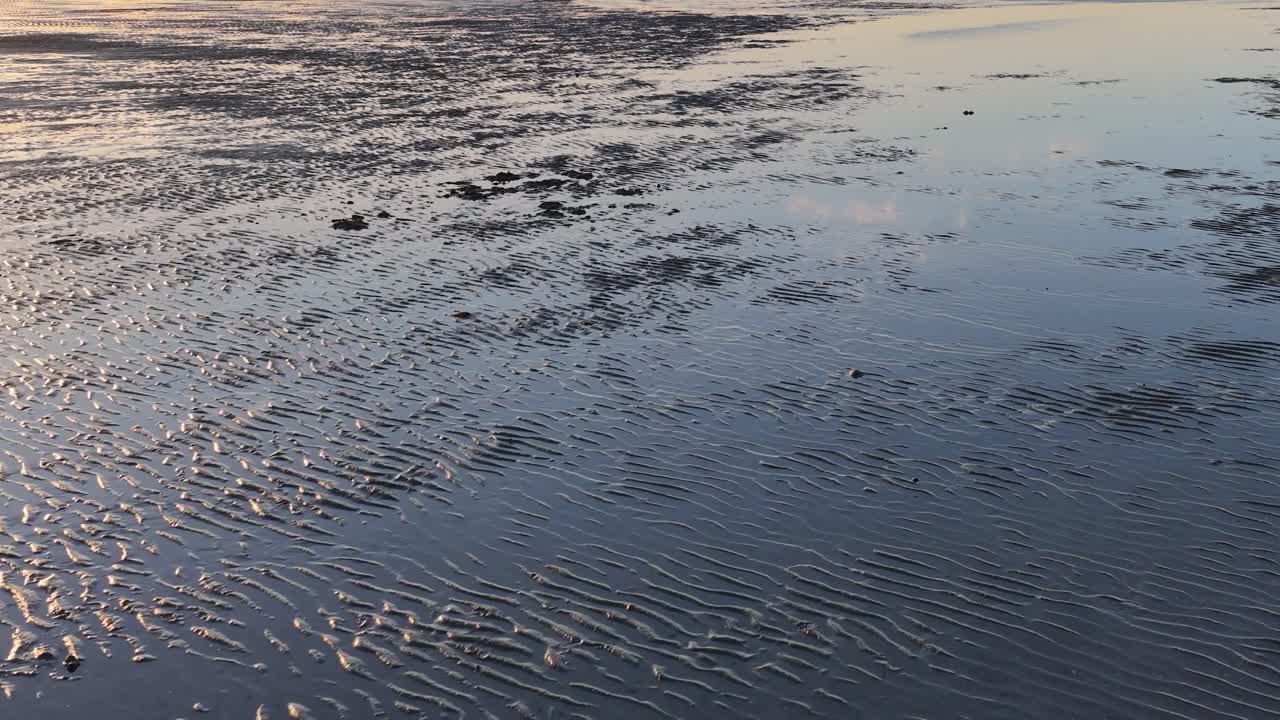 High angle drone shot glides over reflective sandbars and calm bay water at sunset