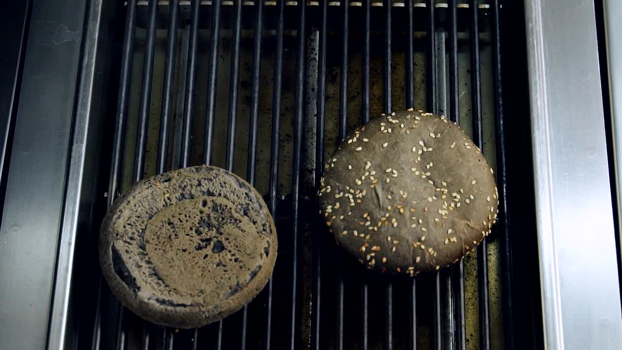 Black bread for hamburber is grilling. Chef putting halves of brown bun on hot grill. Cooking burger. Fast food restaurant
