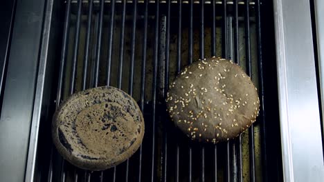 Black bread for hamburber is grilling. Chef putting halves of brown bun on hot grill. Cooking burger. Fast food restaurant