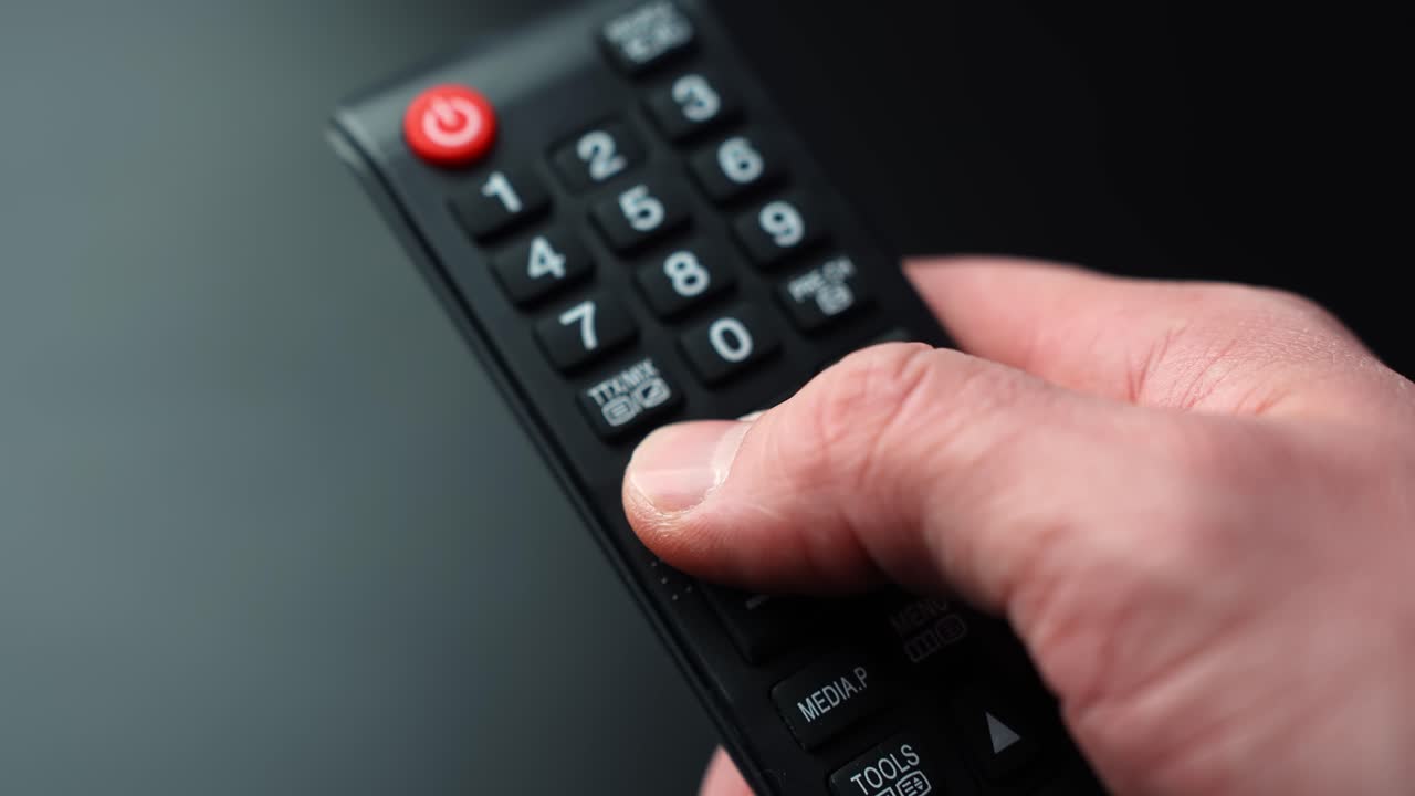 Nahaufnahme einer Hand, die die Lautstärke auf einer TV-Fernbedienung auf dunklem Hintergrund mit geringer Tiefenschärfe und Freiraum für Text erhöht, perfekt für Heimkino- und Streaming-Konzepte