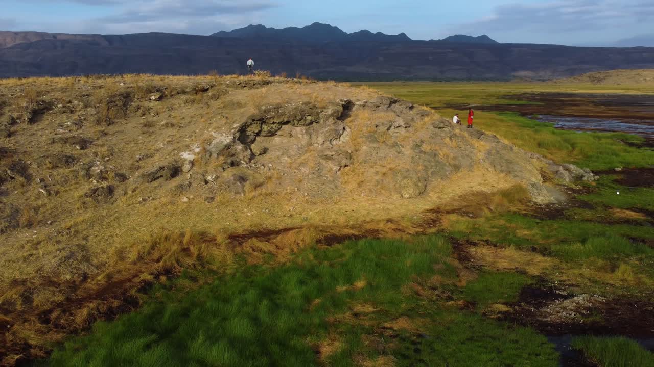 북아프리카의 맑고 푸른 날 배경에 인상적인 산들을 배경으로 언덕 꼭대기에 서 있는 사람들과 함께 탄자니아에 있는 나트론 호수의 아름다운 풍경을 드론으로 촬영했습니다.