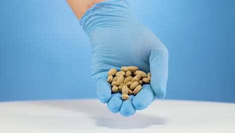 hand with blue gloves shows handful of painkiller tablets with blue backdrop