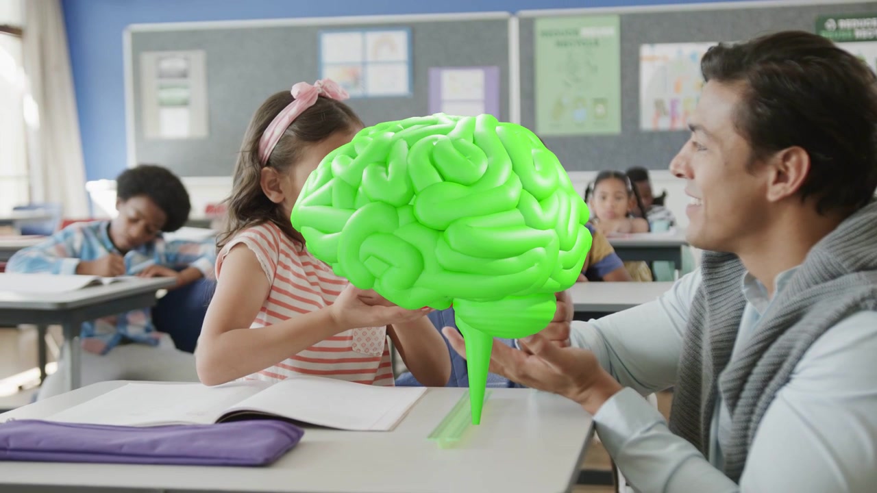 Teacher holding 3D brain in classroom, girl reaching and rotating red green hemispheres for science