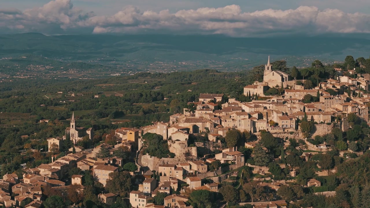 Ripresa aerea che gira a sinistra su Bonnieux, Francia, catturando il villaggio illuminato dal sole e i dintorni lussureggianti.