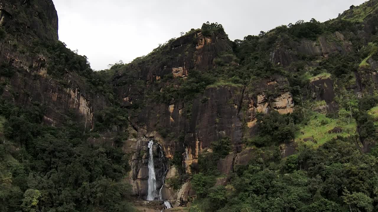 drone aéreo de altos acantilados rocosos y cascada de ravana falls con árboles verdes en ella sri lanka