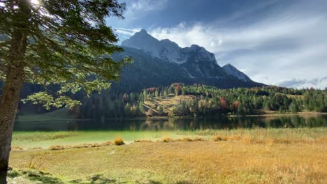 panning shot of the ferchen lake with the golden autumn forest and grünkopf mountain in the background, very close to the bavarian town of mittenwald in germany