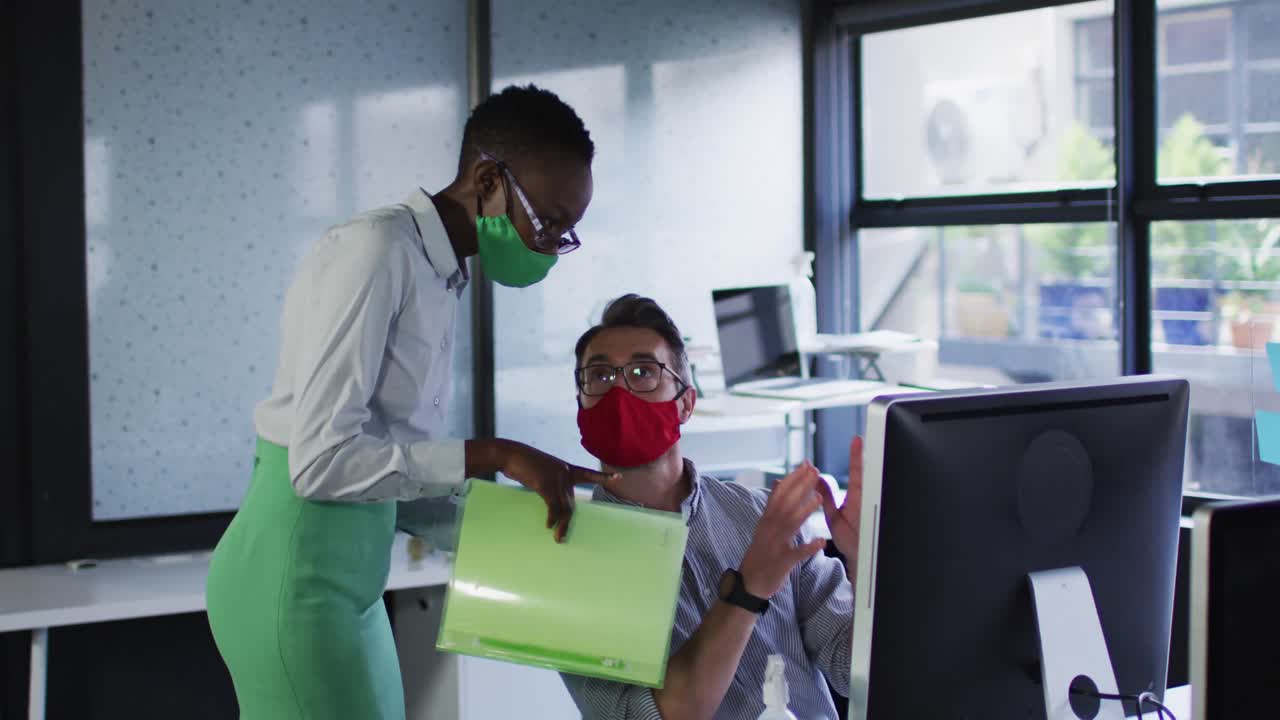 Diverse male and female office colleagues wearing face masks discussing at modern office