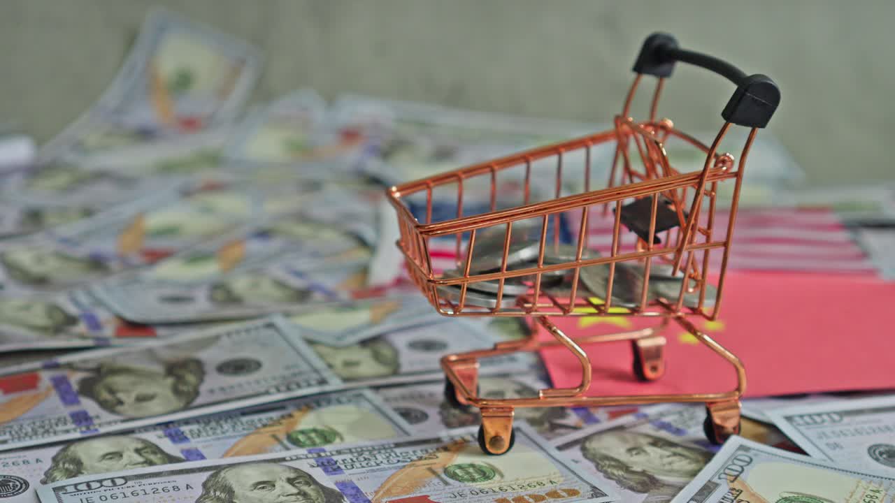Munten vallen in een winkelwagen met op de achtergrond honderd dollarbiljetten.