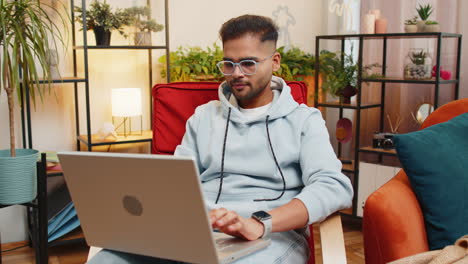 indian young man freelancer starts working on laptop sends messages makes online purchases at home