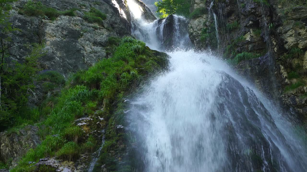 Water falls furiously from the high mountains through rocks and green vegetation in waterfall of Theth, Albania