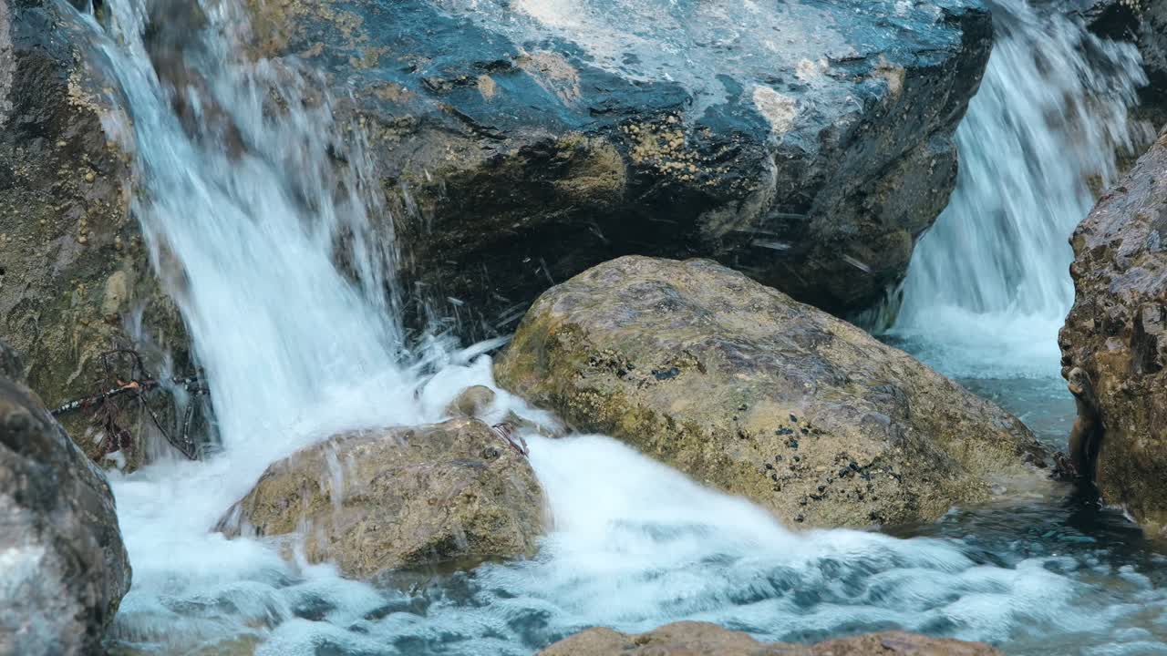 Static image of crystal-clear water cascading over stones from a small waterfall.