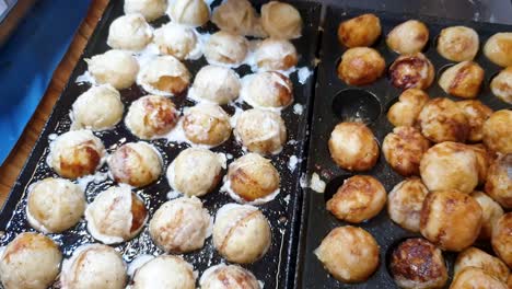 cooking freshly made takoyaki japanese octopus balls, close up of popular street food snack in japan sizzling on a hot plate