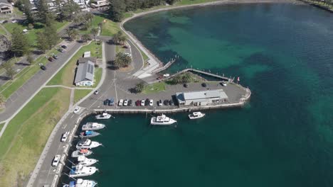 drone orbits above harbor and dock with speedboats tied up to slip in cove, kiama nsw australia