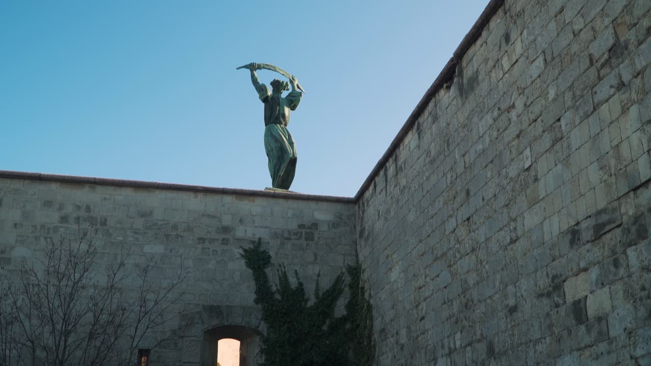 The Concrete Brick Wall In Budapest Hungary With Above Statue Of A Man Holding His Sword Under The Bright Blue Sky - Wide Shot
