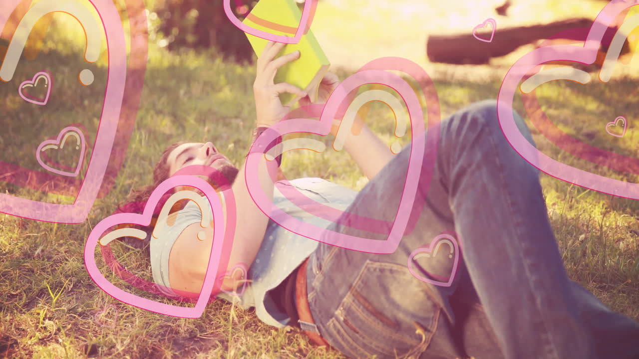 Person lying on grass reading book with pink heart animation overlay