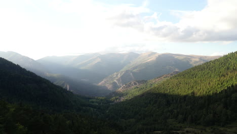 drone shot: slow pan over mountain range with a tree in front and sun rays shining over mountains