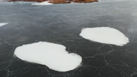 Snow-patches-on-frozen-lake-surface-in-Nordic-landscape,-aerial