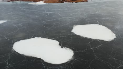 snow patches on frozen lake surface in nordic landscape, aerial