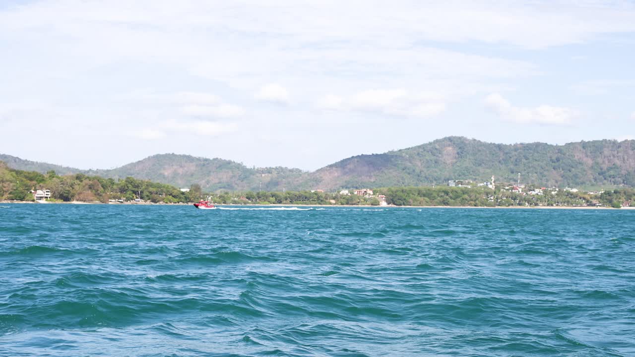 태국 푸켓 근처에서 촬영된 은 하늘 아래의 조용한 바다 풍경, 부드러운 파도와 멀리 있는 언덕