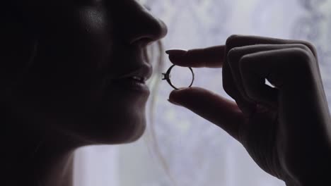 Bride-in-night-gown,-veil-with-engagement-ring-near-window.-Face-close-up-smiling.-Wedding-morning