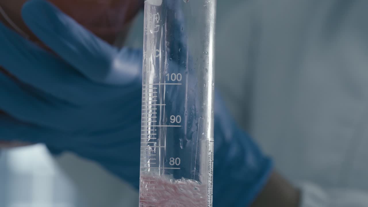 Close up of worker's hand pouring serum liquid into Measuring Tube while working in Medical Drug Production Laboratory