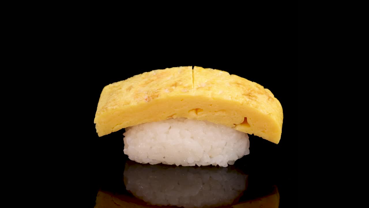 Tamago egg sushi rotates smoothly on a glossy black surface, illuminated by soft studio lighting, highlighting texture and detail in a seamless motion