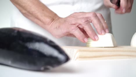persona caucásica mayor cortando cebolla con un cuchillo en una tabla de cortar de madera, pescado en primer plano desenfocado