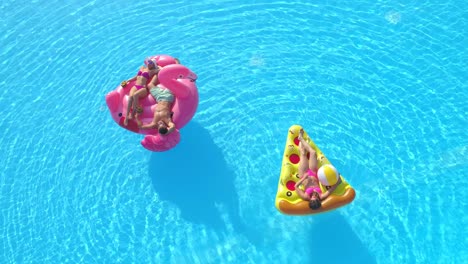 aerial: three friends relax on colorful floaties during carefree summer vacation