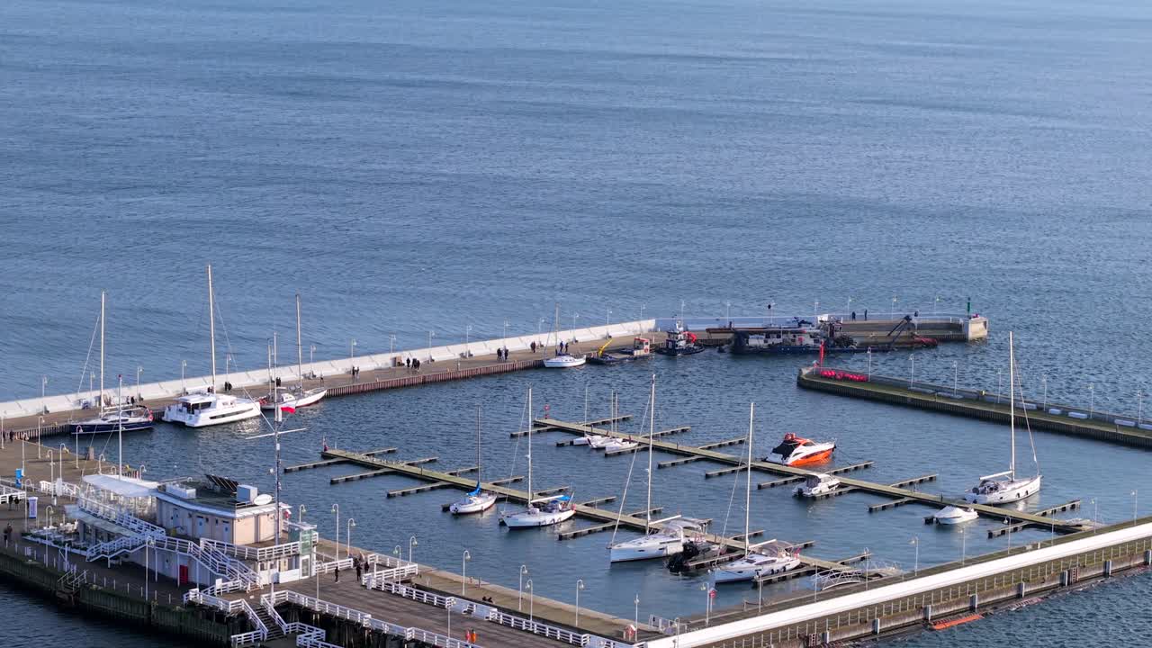 Aerial flyover of Sopot Marina in winter with boats in Baltic Sea, shimmering water under a sunny day