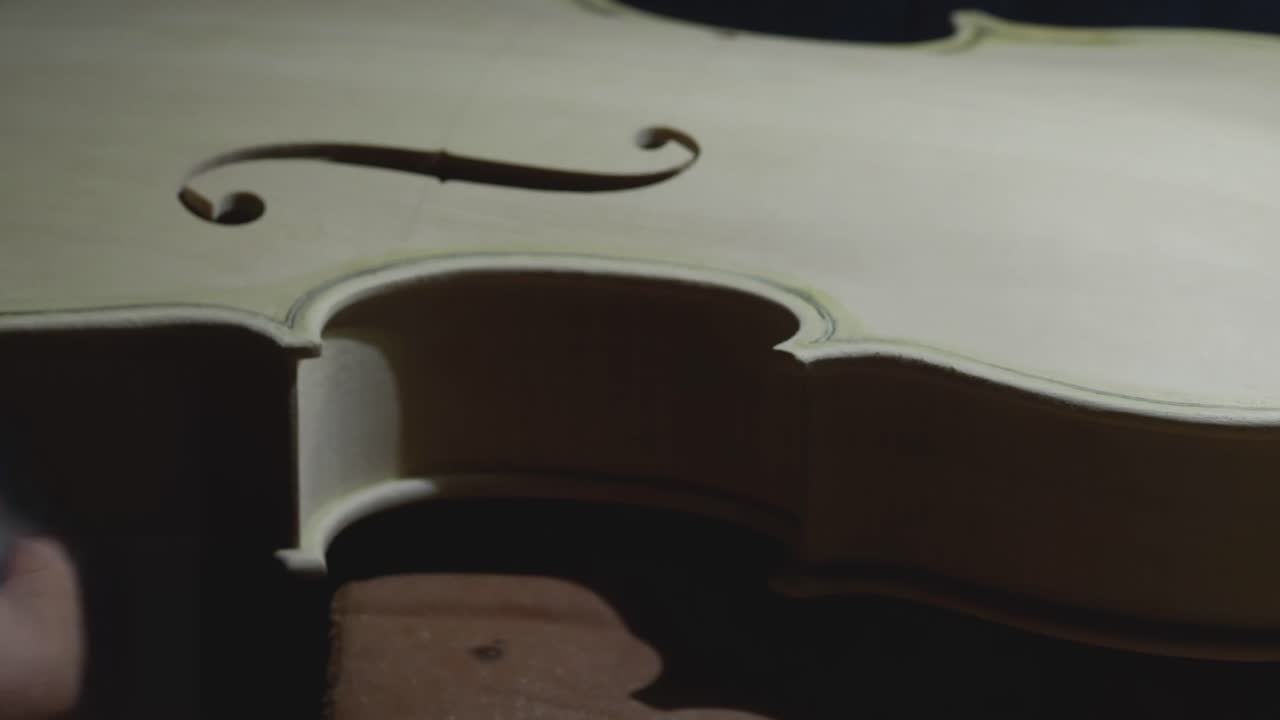 Skilled luthier carefully shaping delicate f-hole of violin using precise hand tools, showcasing intricate woodworking craftsmanship in traditional instrument-making process