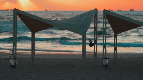 Toma-En-Cámara-Lenta-De-Un-Hombre-Joven-Haciendo-Un-Giro-Frontal-En-La-Playa-Al-Atardecer,-Hora-Dorada