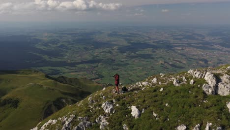 Circling-shot-of-a-young-man-standing-by-himself-alone,-taking-photos-with-his-camera-of-the-vast-and-majestic-landscape-in-front-of-him