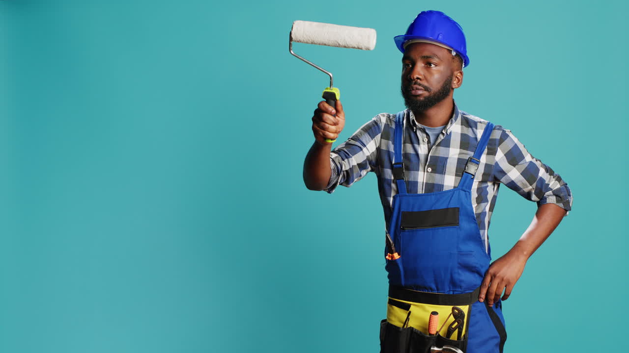 Repairman in overalls painting walls with roller brush