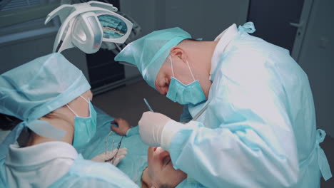 stomatologist man is sewing with thread in patient's mouth in dental clinic. specialist man and his assistant in medical uniform working together with a patient indoors. dental operation.
