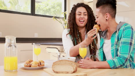 una pareja de lesbianas sonrientes desayunando juntos en la cocina.