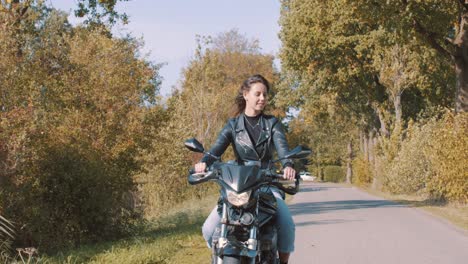 Una-Joven-Sonriente-En-Motocicleta-Recorriendo-Bosques-Y-Campos-Rurales-Con-árboles-Dorados-De-Hojas-De-Otoño-En-Un-Día-Soleado