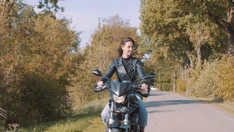 jovencita sonriente en motocicleta recorriendo bosques y campos rurales con árboles dorados de hojas de otoño en un día soleado
