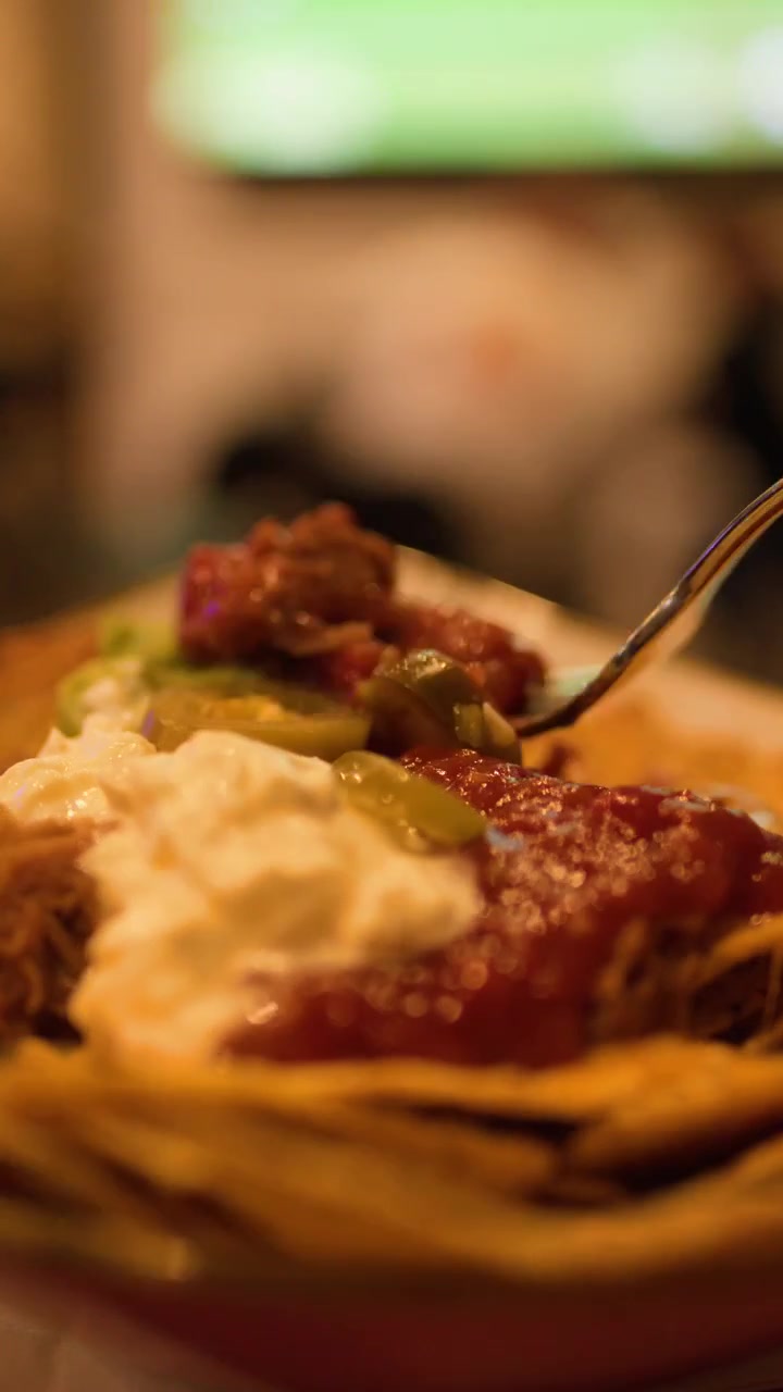 Primo piano di una forchetta che solleva nachos con salsa e panna acida