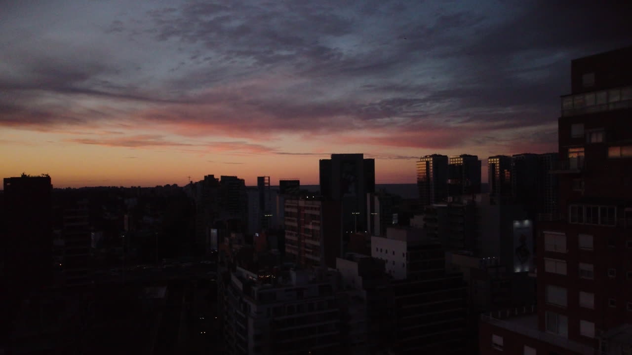Dron permanece inmóvil sobre la ciudad al atardecer, cielo azul rosado, frío