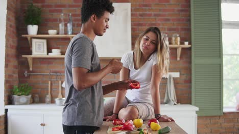 Glückliches-Multiethnisches-Paar,-Das-Sich-Frühmorgens-In-Der-Küche-Unterhält.-Schöner-Mann,-Der-Seine-Frau-Füttert,-Während-Er-Das-Frühstück-Kocht