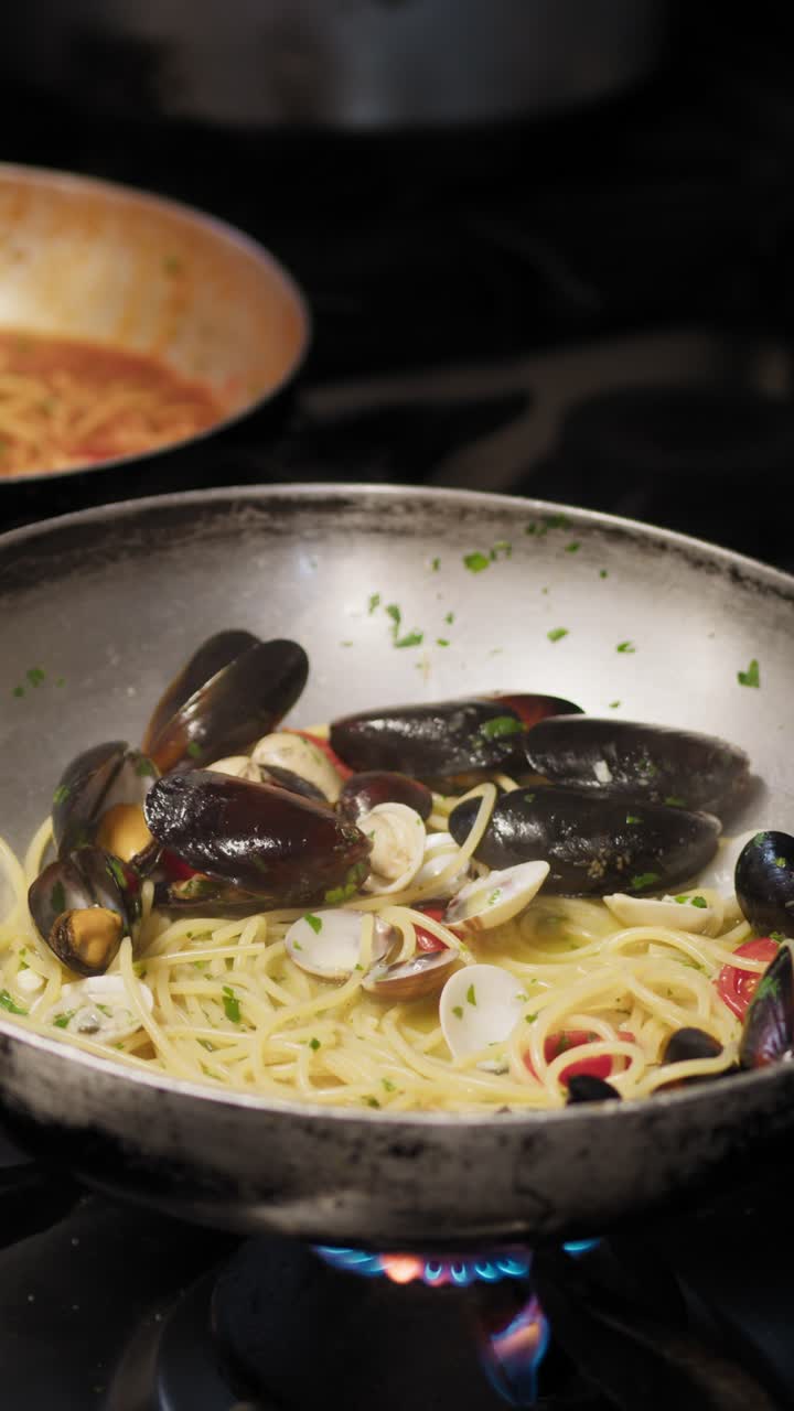 Chef che usa diverse padelle mentre cucina pasta ai frutti di mare.