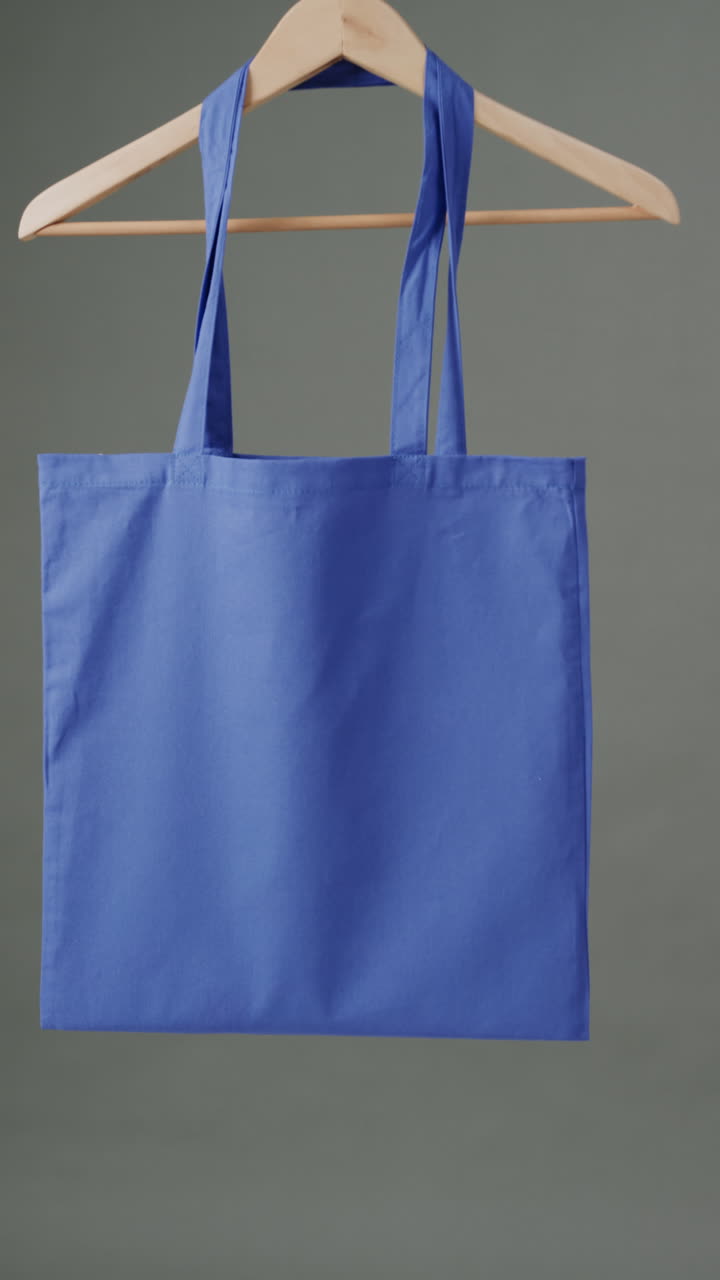 Vertical video of hanger with blue canvas bag and copy space on grey background