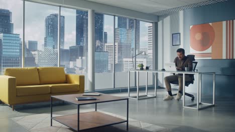 portrait of thoughtful middle eastern businessman sitting at his desk working on laptop computer in big city office. successful digital entrepreneur doing data analysis for e-commerce startup