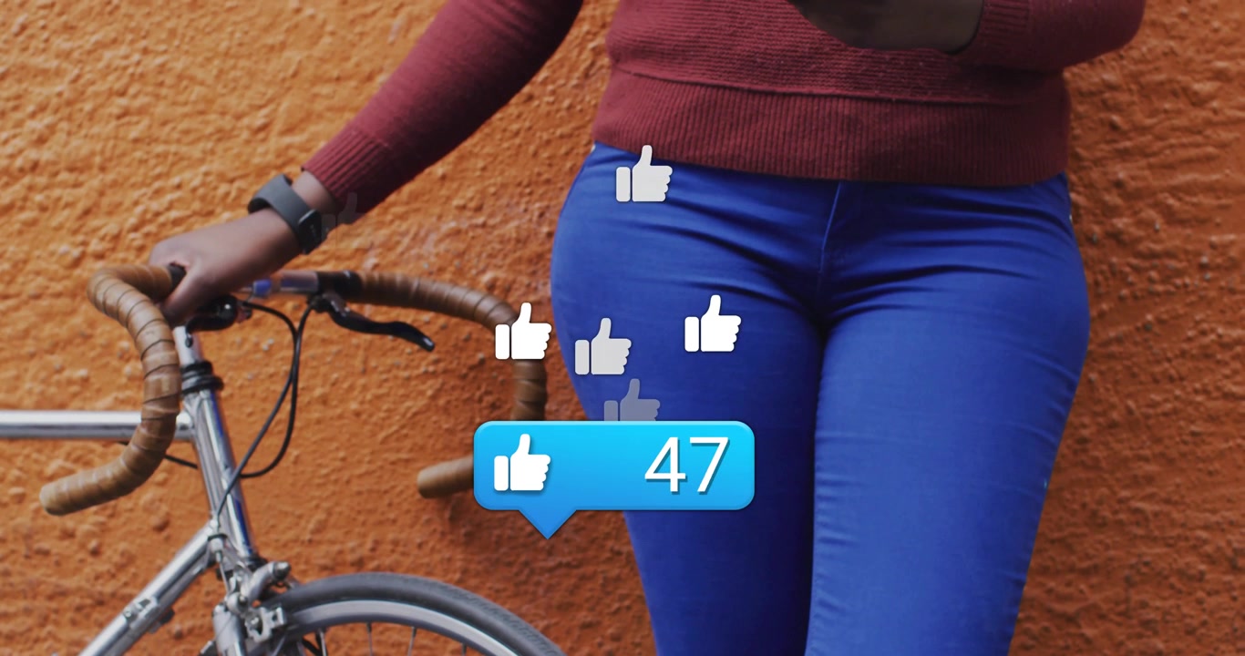 Mulher encostada com bicicleta em parede laranja, verificando balão de notificação enquanto curtidas em redes sociais aumentam