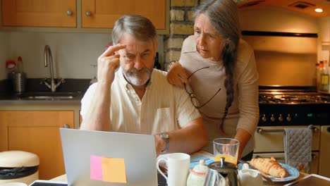 front view of old caucasian senior couple discussing over laptop in a kitchen 4k