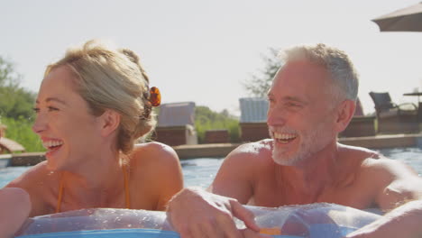 smiling multi-generation family on summer holiday relaxing in swimming pool on airbed
