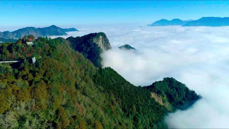 Spectacular-aerial-view-showing-green-growing-mountains-outstanding-between-white-cloudscape-in-summer