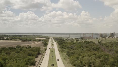 Vehicles-travel-along-a-two-sided-highway-near-a-growing-lake-side-factory-town